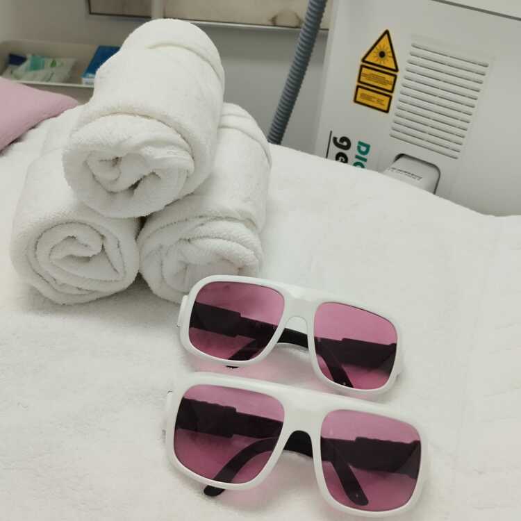 Weiße Sonnenbrillen mit rosa Gläsern liegen neben einem Stapel sauberer, gefalteter Handtücher auf einem weißen Handtuch.