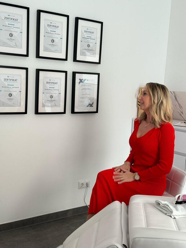 Eine Frau in einem roten Kleid sitzt in einem modernen Raum mit gerahmten Zertifikaten an der Wand.